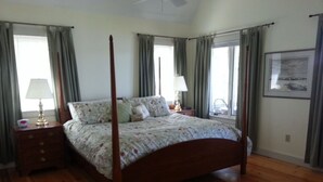 Een hemelbed met bloemenbedrukking, een nachtkastje met lamp, en een ingelijst foto aan de muur.