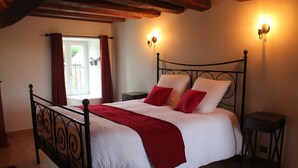 Ein Schlafzimmer mit einem Bett, zwei Nachttischen, einem fensterbelaubten Fenster und Wandleuchten.