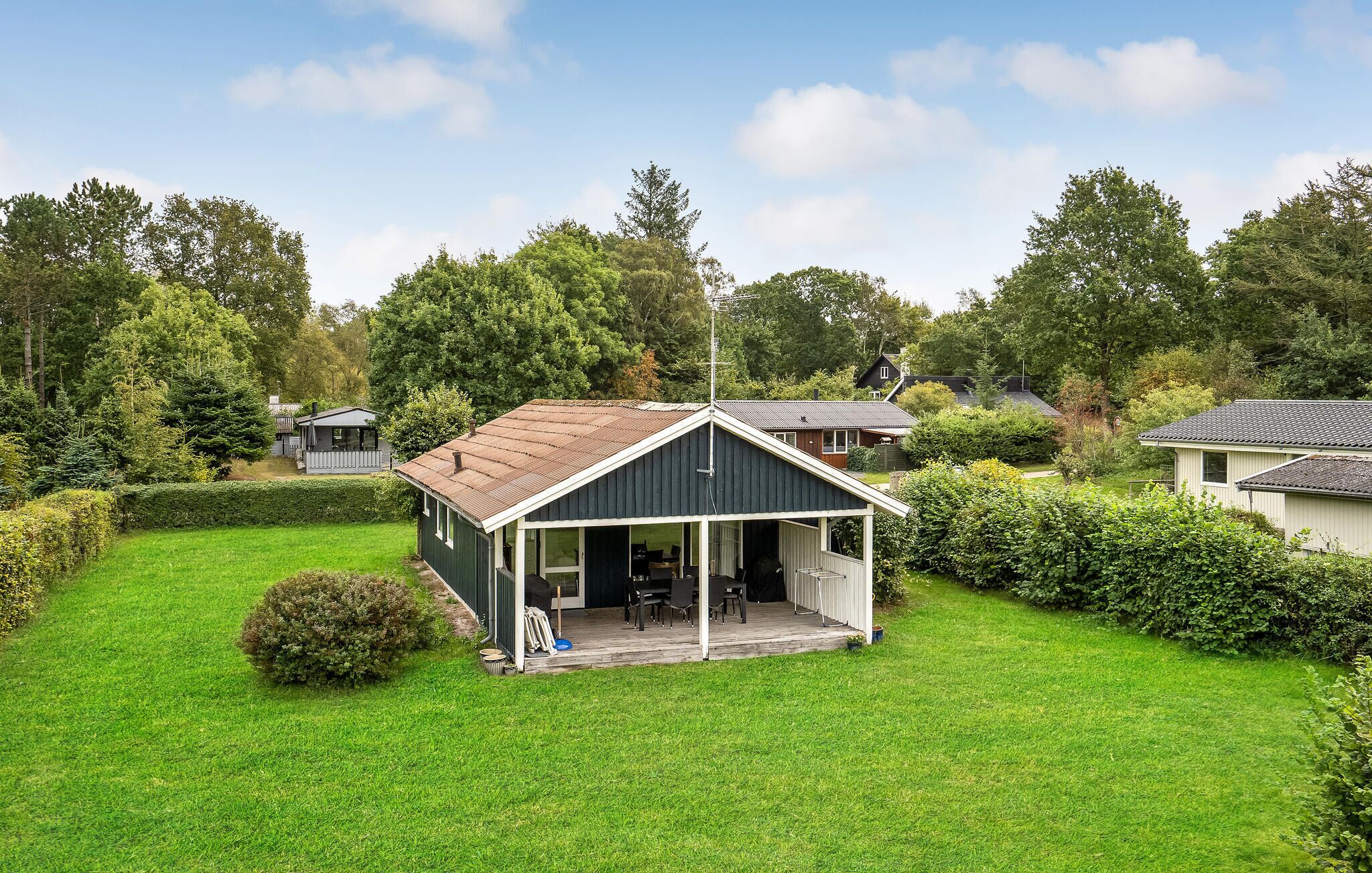 Una piccola casa a un piano con veranda e zona relax esterna coperta.