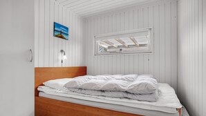 A bedroom with a wooden headboard, a bed with white bedding, a wall-mounted lamp, a small painting, and a window with a view of the sky. - 3 bedroom nice home in Glesborg (Glesborg)
