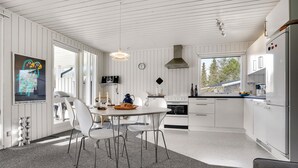 A modern kitchen with white cabinetry, a dining area with a round table and chairs, a large window, and a view of trees outside. - 3 bedroom nice home in Glesborg (Glesborg)