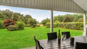 A covered patio with a table set for two, overlooking a well-maintained lawn and garden. - 3 bedroom nice home in Glesborg (Glesborg)