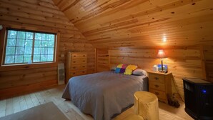 Camera da letto in una baita di legno, con un letto, una cassettiera, una lampada, un termosifone e una ventola a soffitto.