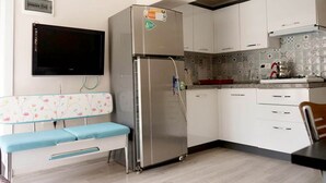 Una cucina compatta con frigorifero integrato, una TV a schermo piatto montata a parete e una panca con rivestimento floreale.