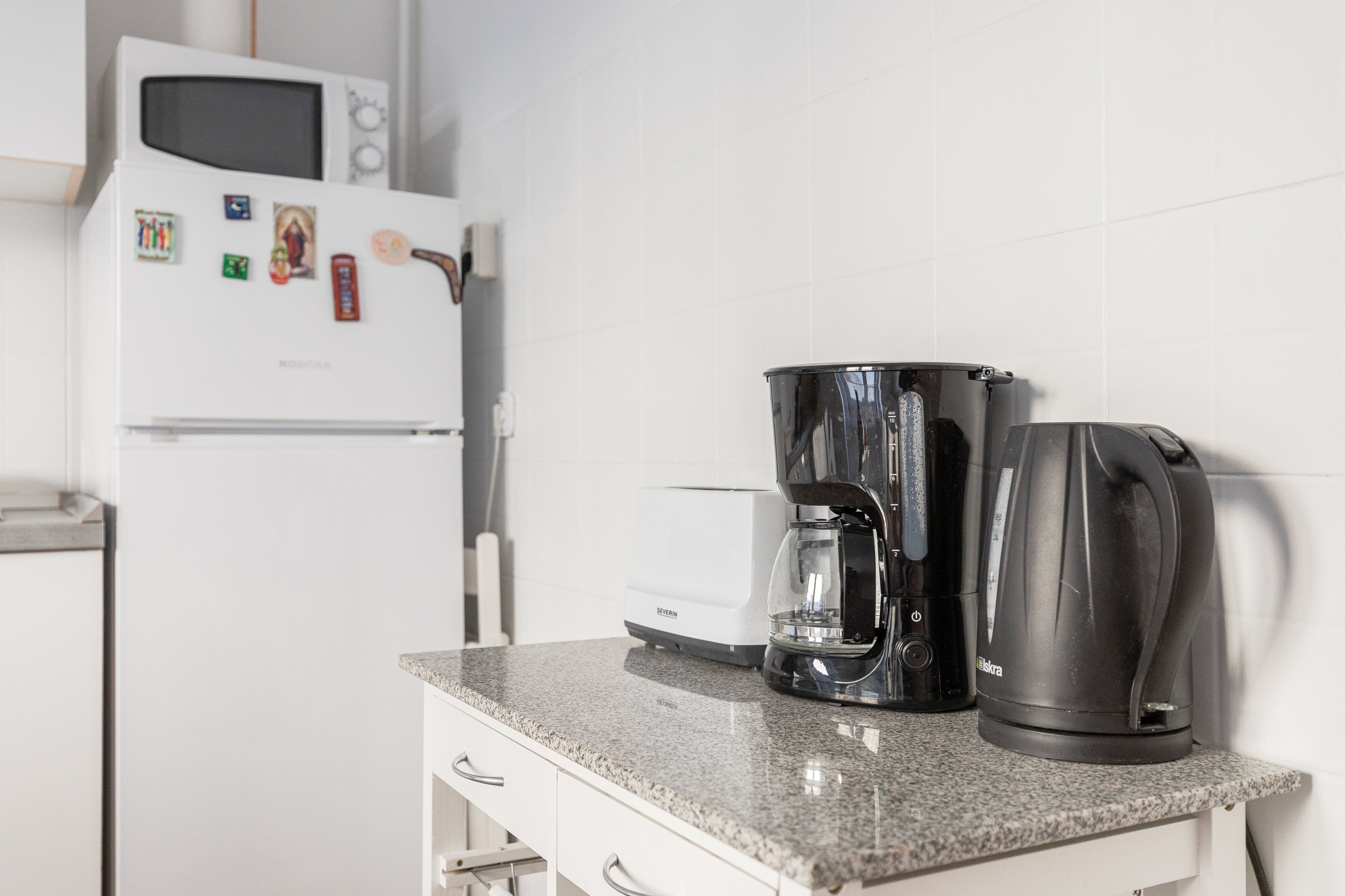 Una cocina con microondas, cafetera y hervidor eléctrico sobre una encimera de granito.