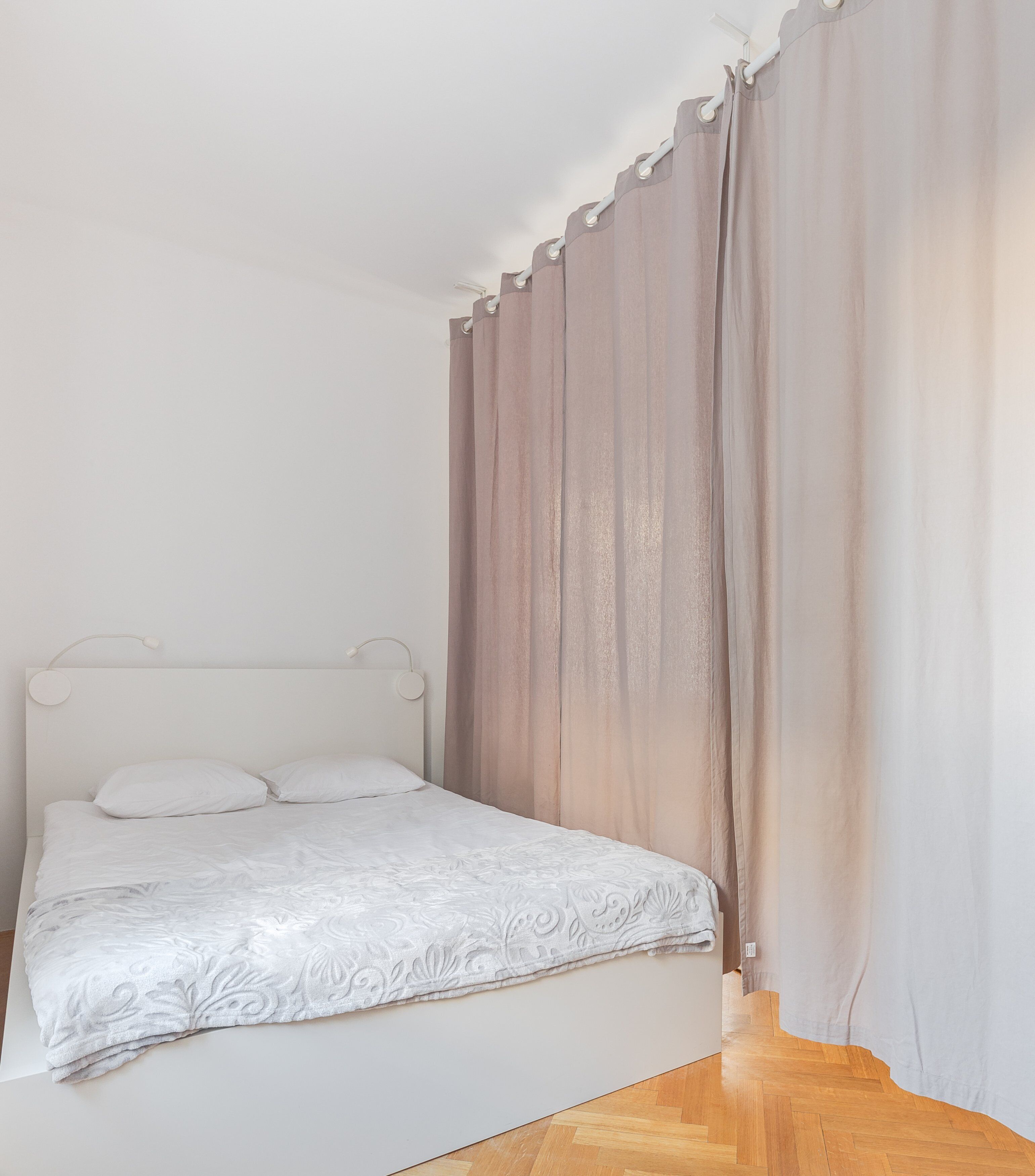 A bedroom with a bed, white headboard, and curtains.