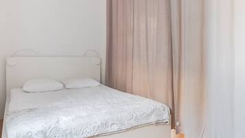 A bedroom with a bed, white headboard, and curtains.