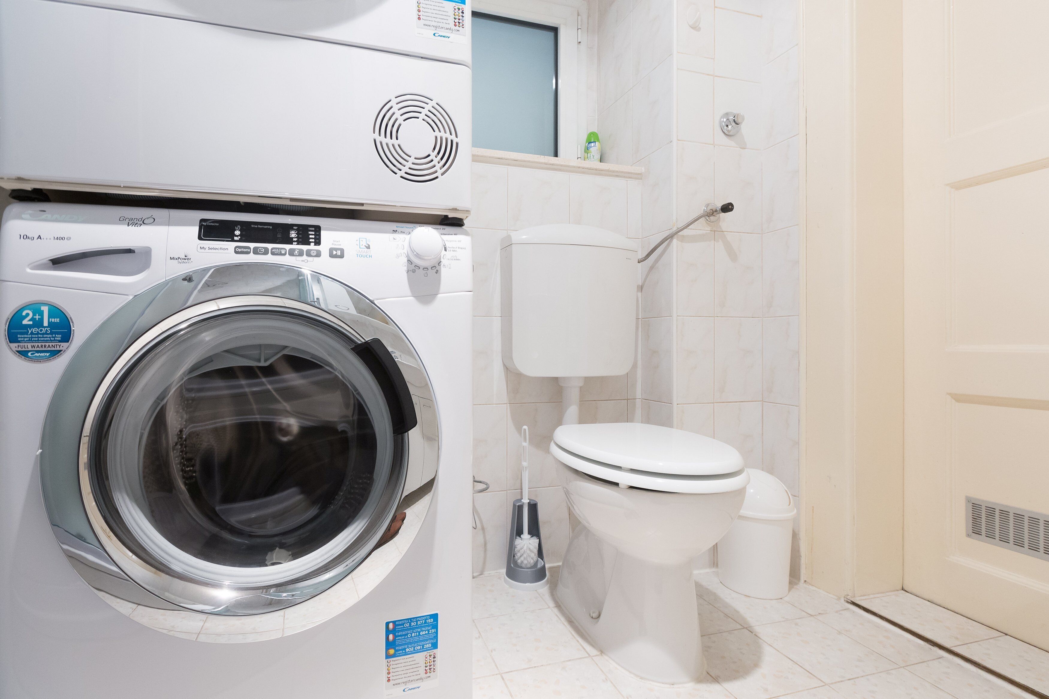 A front view of a washing machine and a toilet in a bathroom.