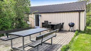 A wooden deck with a picnic table and chairs, a barbecue grill, and a shed with a tiled roof. - 3 bedroom stunning home in Anholt (Anholt)