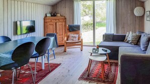 A cozy living room with a wooden interior, a dining table with chairs, a sofa, and a TV mounted on the wall. - 3 bedroom stunning home in Anholt (Anholt)