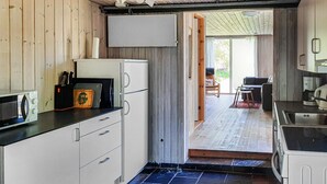 A compact kitchen with white cabinets, a black countertop, and a small refrigerator. There is a wooden door leading to a dining area with a table and chairs. - 3 bedroom stunning home in Anholt (Anholt)