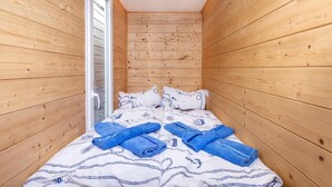 Une petite pièce en bois avec un lit, des oreillers et des serviettes pliées.