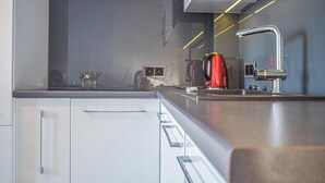 Moderni keittiö, jossa on valkoiset kaapit, ruostumattomasta teräksestä valmistettu työtaso ja punainen vedenkeitin.
