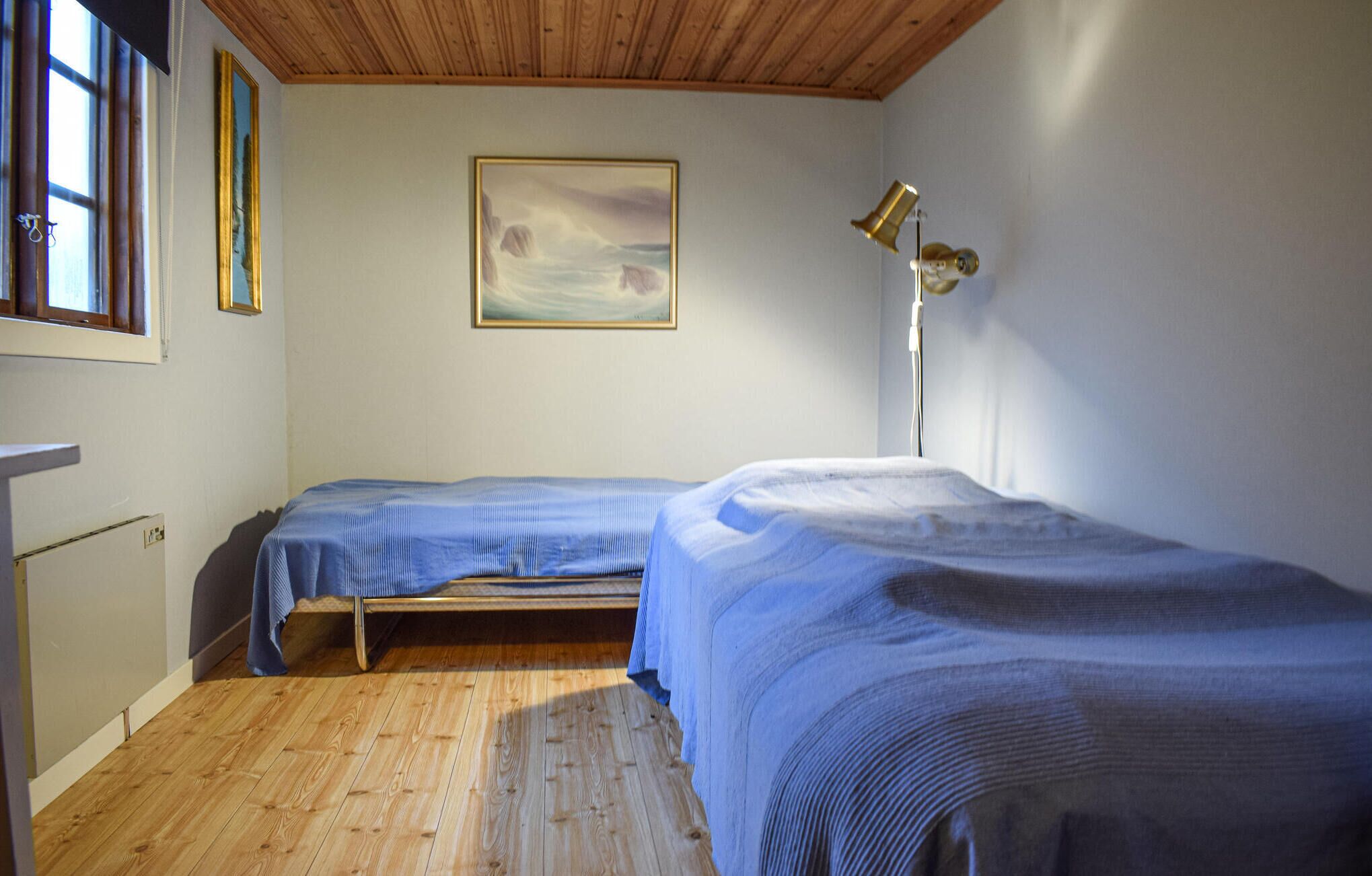 Un dormitorio con dos camas individuales, techo de madera, un cuadro en la pared y una lámpara de pie.
