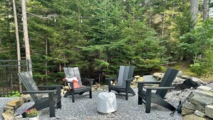 Un espacio al aire libre con sillas Adirondack, una fogata y un camino de piedra.