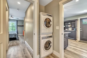 A laundry room with a stacked washer and dryer, a ceiling fan, and a window with curtains.