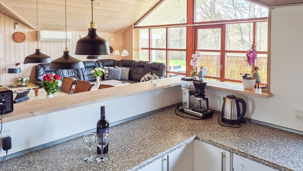 Cozinha moderna com forno embutido, cafeteira e área de jantar com sofá e mesa.