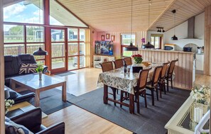 A spacious living area with a large TV, wooden furniture, and a dining table with chairs.