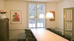 A conference room with a long table, chairs, a vase with flowers, a framed picture, and a window with frosted glass. - Nice home in Gusum with lake view (Gusum)