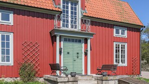A red wooden house with a green door, two windows, and a balcony with metal railings. - Nice home in Gusum with lake view (Gusum)