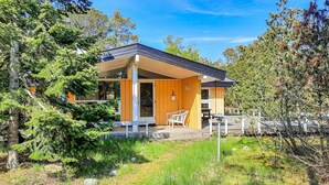 Ein modernes Haus mit einer überdachten Terrasse, umgeben von Bäumen und einer Rasenfläche.