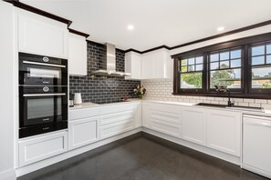 A modern kitchen with white cabinetry, a Bosch oven, a black tiled backsplash, and a window with a view of the outside.