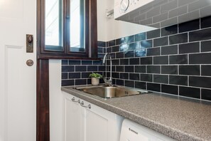 A kitchen with dark tiled backsplash, a stainless steel sink, and white cabinets.