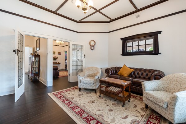 A living room with a brown leather sofa, patterned armchairs, a wooden coffee table, and a red and white patterned rug.