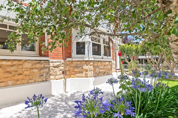 A stone wall with a window, a white railing, and a garden with blue flowers.