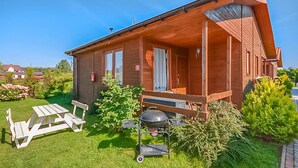 A wooden cabin with a porch, a barbecue grill, and a picnic table. - 2 bedroom amazing home in Wicie (Wicie)