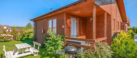 A wooden cabin with a porch, a barbecue grill, and a picnic table.
