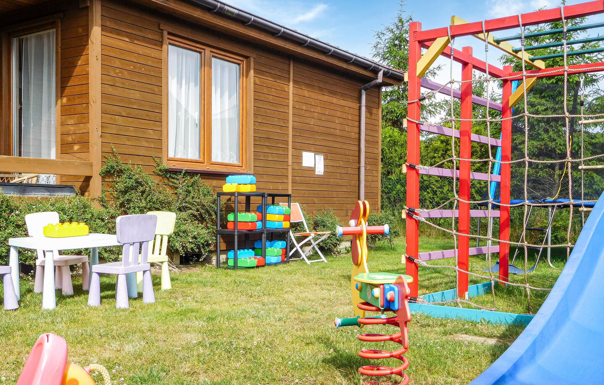 Une maison en bois avec un espace de jeux comprenant un toboggan, une structure d’escalade et une table avec des chaises.