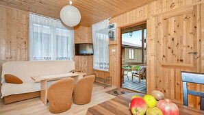 A wooden cabin interior with a sofa, chairs, a dining table with fruit, and a TV. - 2 bedroom amazing home in Wicie (Wicie)