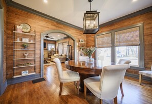 A dining area with a wooden table, white upholstered chairs, and a hanging lantern.