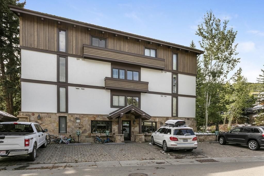 A modern building with a stone base and wooden upper floors, featuring a central entrance with a small porch.