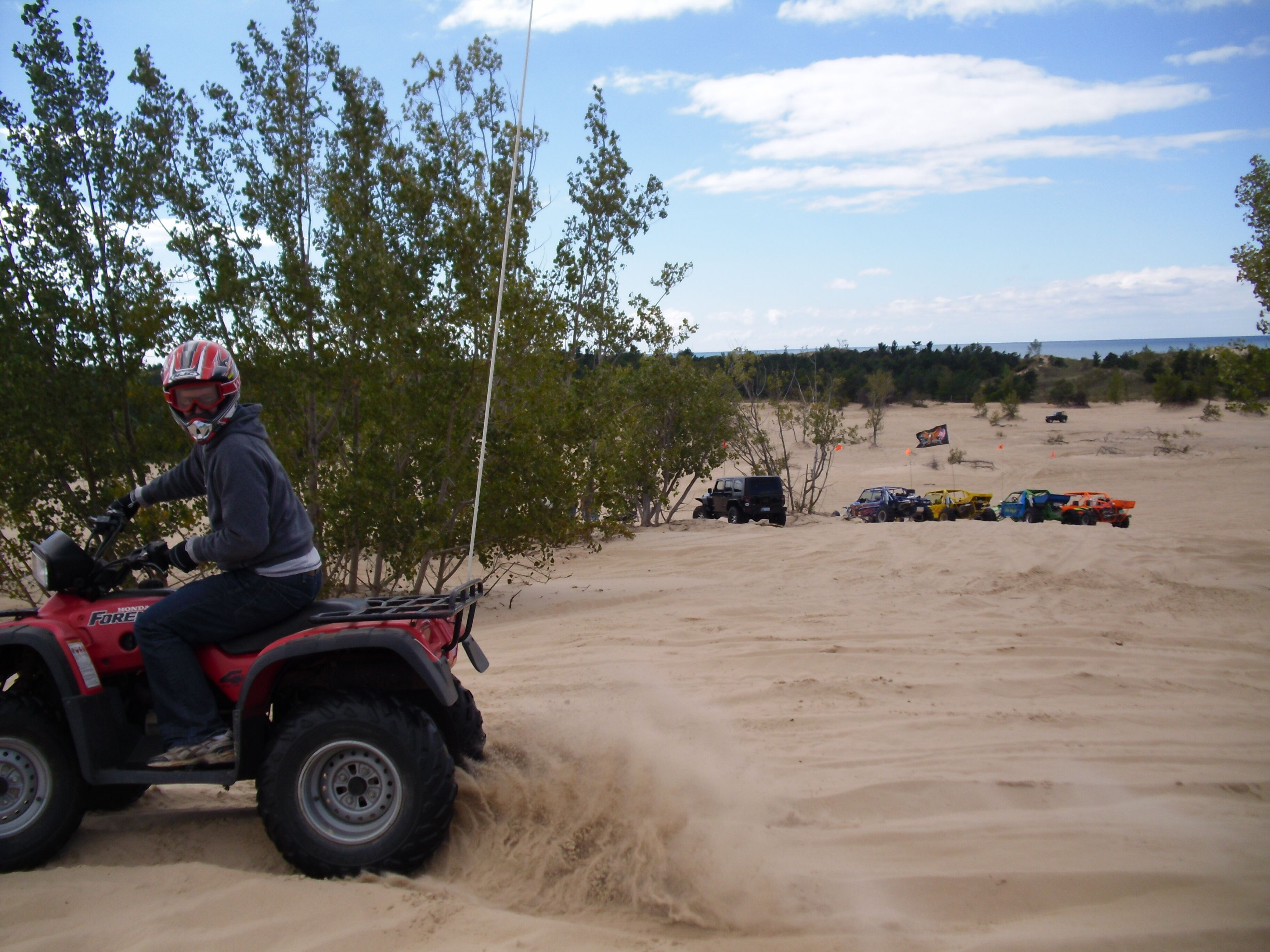 A person riding a red Honda Forester ATV in a sandy area with trees and a clear sky.