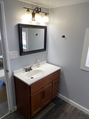 Un baño con lavamanos blanco, tocador de madera y un espejo grande con tres luces.