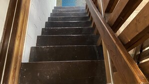 Una escalera de madera con barandilla negra que lleva a un rellano con una silla negra.