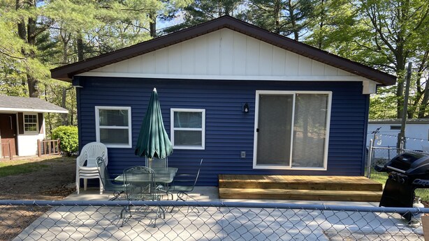 Una casa pequeña con fachada azul, un porche techado con sillas y una terraza de madera.