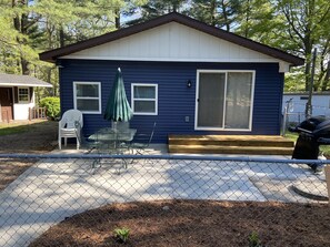 Una casa pequeña con fachada azul, un porche techado con sillas y una terraza de madera.