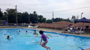 Una piscina con gente en el agua y en el borde.