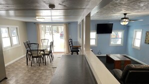 Amplia sala de estar con una barra alargada, una mesa de comedor con sillas, un sofá y un ventilador de techo.
