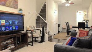 Una sala de estar con televisión, una escalera, un comedor y un sofá.