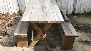 Una mesa de picnic de madera con bancos, frente a una cerca blanca.