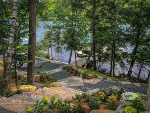 Un jardin paisible au bord du lac, avec des allées pavées de pierres, une végétation luxuriante et une jetée qui s’avance sur l’eau.