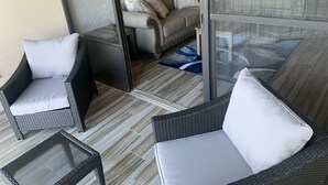Ein Balkon mit Korbmöbeln, einem Glastisch und einer Couch mit Kissen.
