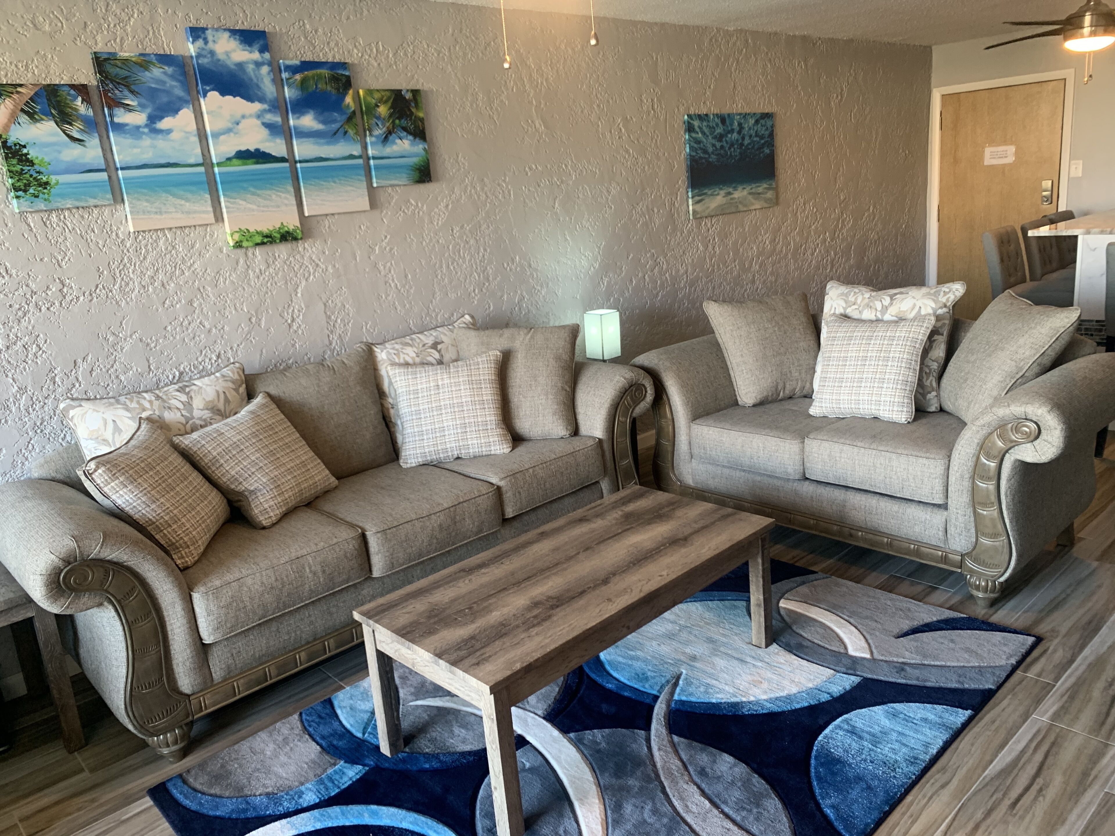A living room with a beige sofa, a wooden coffee table, and a blue patterned rug.