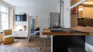 A compact kitchen with a wooden countertop, a white cabinet, and a small dining area with a chair. - Loft Munich Old Town (München)