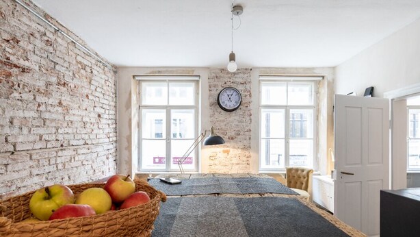 A room with a brick wall, a clock, a basket of apples, and a desk. - Loft Munich Old Town (München)
