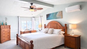 A bedroom with a wooden bed, a desk, a chair, a dresser, a ceiling fan, and an air conditioning unit.